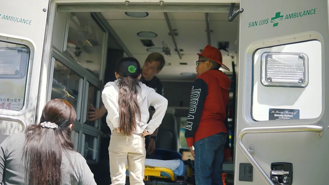 3 children looking inside the back of an ambulance with san luis ambulance personnel looking on.